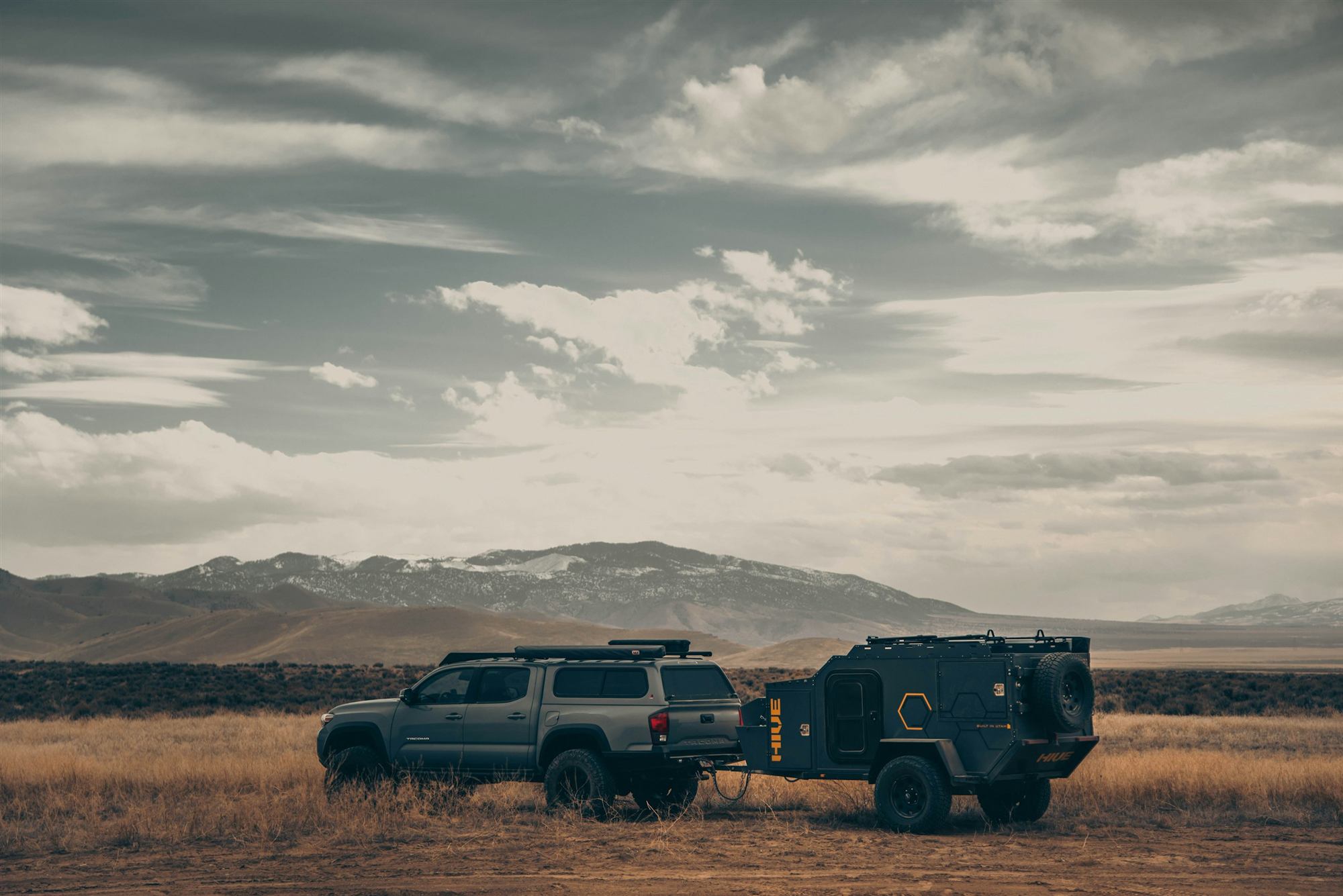 Pickup 4×4 preparada con un trailer off-road en una llanura con la cordillera al fondo